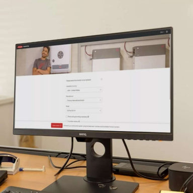 Computer monitor on a desk displays a setup or registration page with images of solar inverters, including the Fronius Primo GEN24 Inverter-3.8kW-4,210,140,800