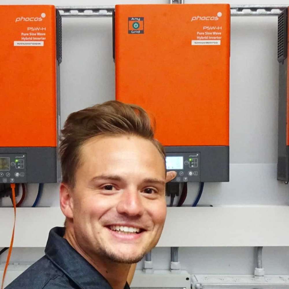 Phocos PSW-H-6.5KW-120/48V 6500 Watt 120VAC Any-Grid Hybrid Inverter/Charger is mounted on a wall behind a technician