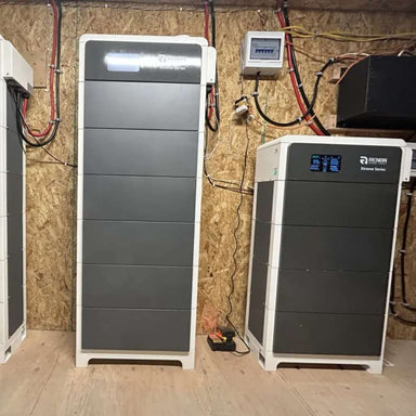 Renon Power Xtreme HV Series 10.24kWh Stackable Battery Module-XTREMEHVBCU is a tall indoor battery cabinet with a front display installed against a wooden utility room wall with visible wiring
