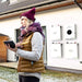 Simpliphi by Briggs & Stratton PHI-1.4-12-T 12 Volt 1.4kWh Lithium Battery is shown in a home energy setup where a person uses a tablet outside a house with wall-mounted power units
