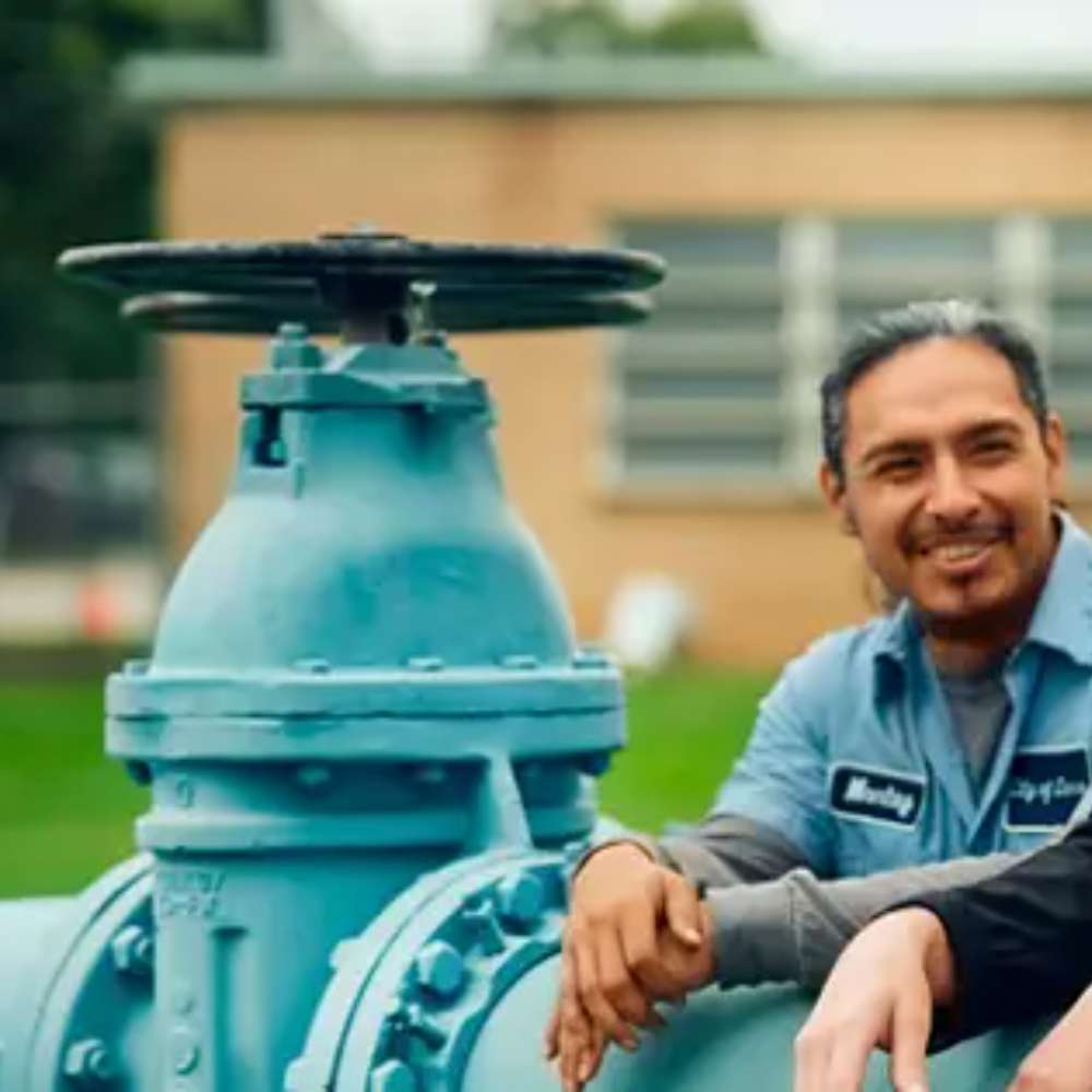 Smiling technician beside a large blue valve illustrates water infrastructure supported by the Grundfos GRFSFSW Float Switch