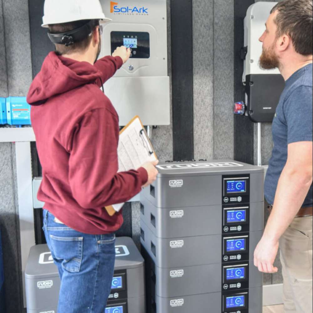 Two men inspect an inverter system above stacked units of the Rubix Stack Series 48 Volt 100AH Lithium Battery-RS-48100