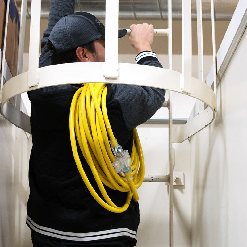 Man carrying a DuroMax 100ft heavy-duty extension cord up a stairwell, illustrating its length and portability