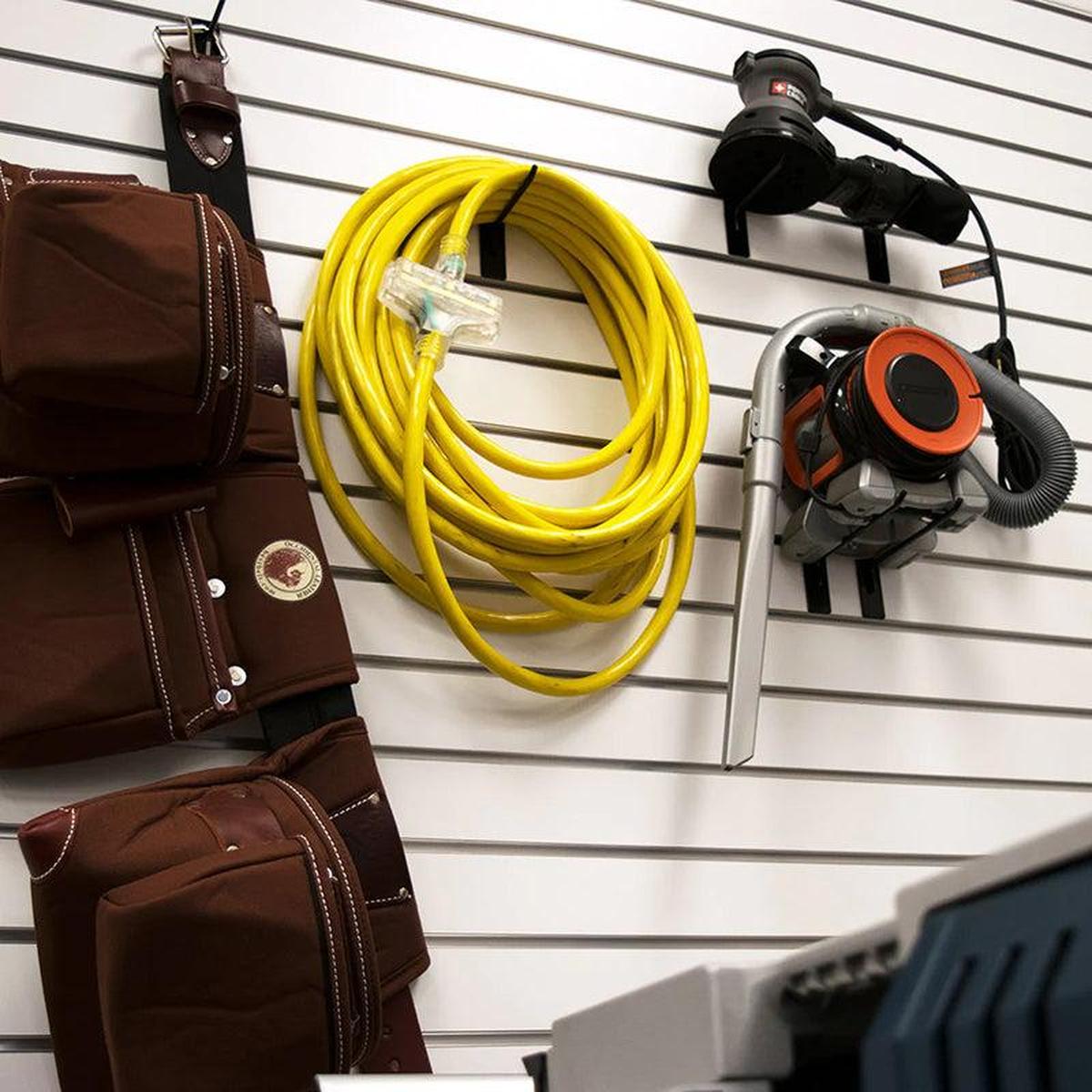 Bright yellow DuroMax extension cord hung on a wall organizer in a workshop, emphasizing storage convenience