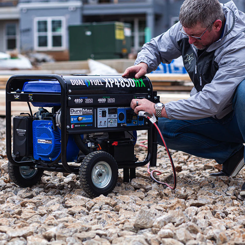 A person crouching to start a DuroMax XP4850HX generator on a construction site, highlighting the generator's ease of use in rugged conditions.