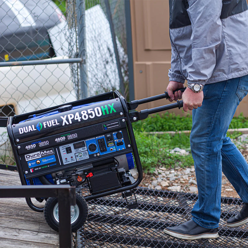 Man pulling a quality DuroMax XP4850HX dual fuel portable generator across a metal grate, demonstrating ease of transport.