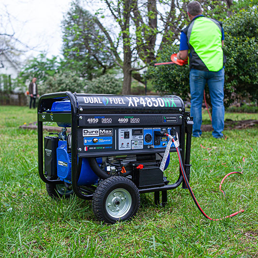 Practical use of a DuroMax XP4850HX generator outside with a person working in the background, highlighting its utility in yard work.