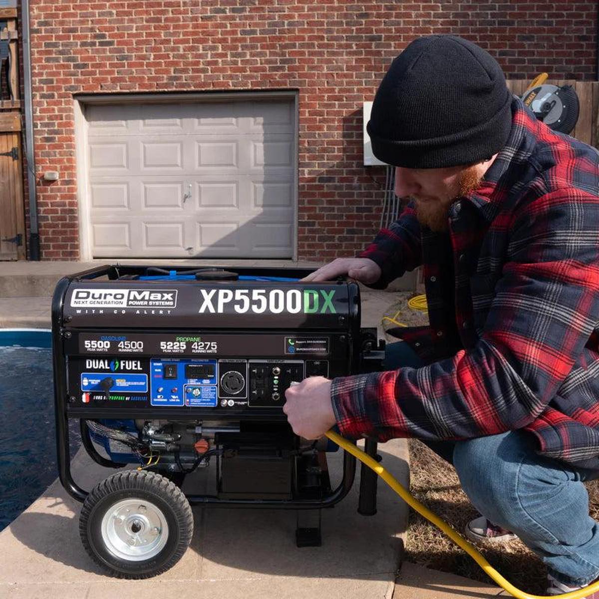 Bearded man in winter attire operating a Duromax XP5500DX portable generator outside a home.