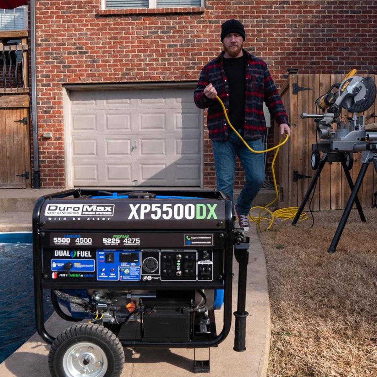 Man with a cable in hand walking away from a stationary Duromax XP5500DX portable generator.