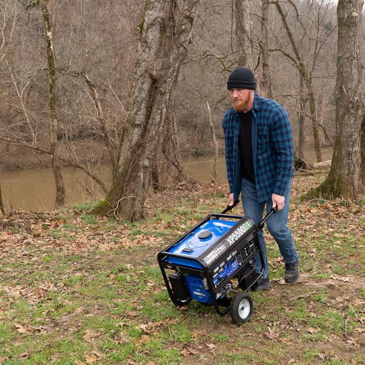 Man pushing a Duromax XP5500DX portable generator through a rustic outdoor environment.
