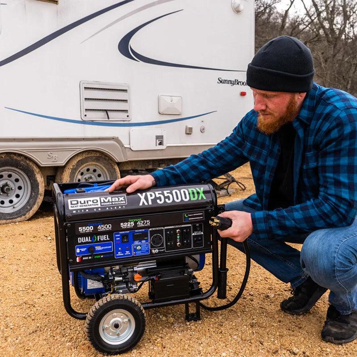 Man setting up a Duromax XP5500DX portable generator next to an RV in a rural area.