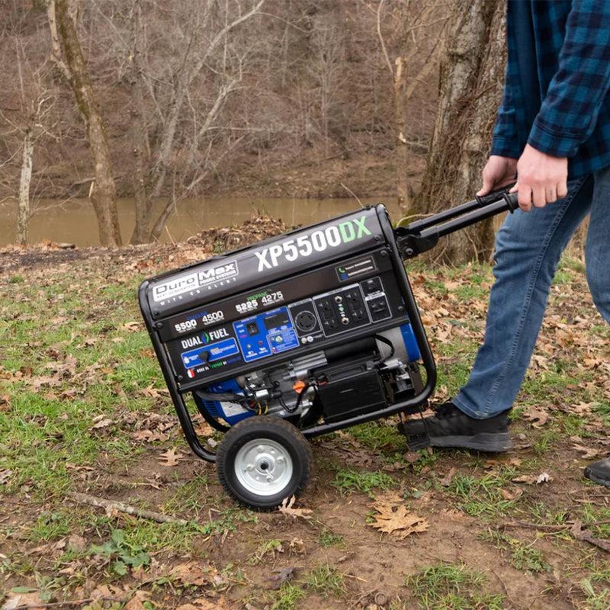 Man pushing a Duromax XP5500DX portable generator through a rustic outdoor environment.