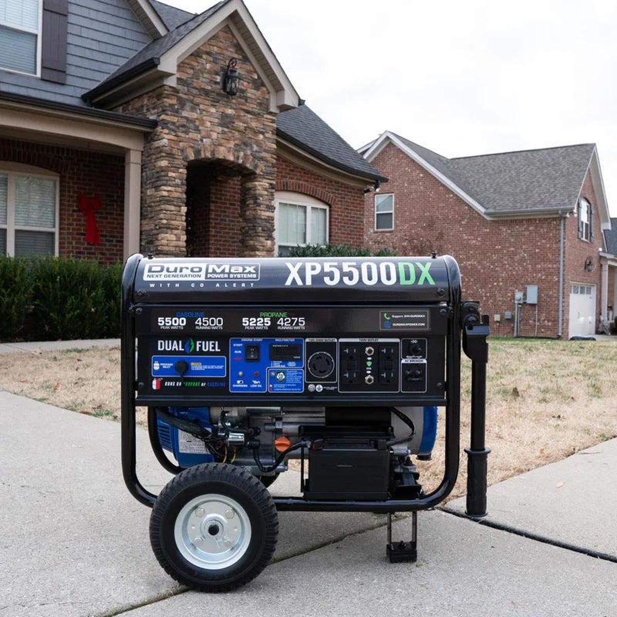 A Duromax XP5500DX portable generator is stationed on a suburban driveway with a brick house in the background, highlighting its suitability for home use and emergency power backup.