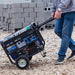 Man maneuvering a Duromax XP5500HX portable generator over rough terrain, showing its durability and easy handling.