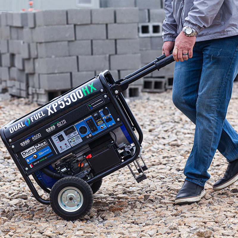 Man maneuvering a Duromax XP5500HX portable generator over rough terrain, showing its durability and easy handling.