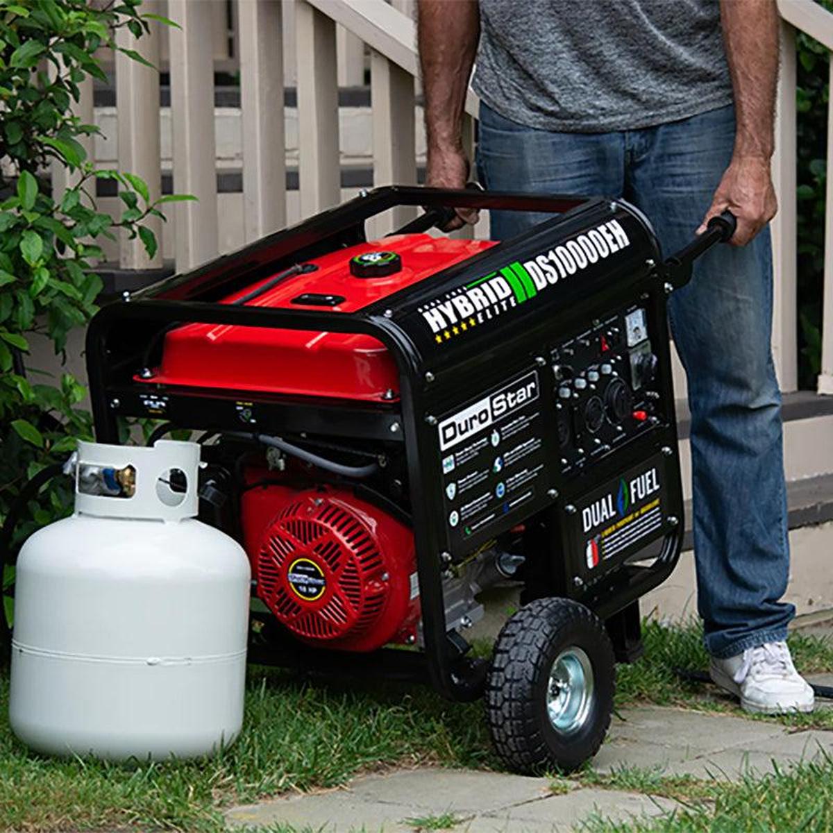 Man easily transporting the DuroStar DS10000EH portable generator with an ergonomic handle, next to a propane tank for dual fuel functionality.