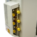 Close-up of a beige metal appliance or machinery component with a side panel removed, showing brass fittings and four bright yellow plastic caps on a white background.